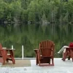 three wooden chairs with on occupied over looking a lake
