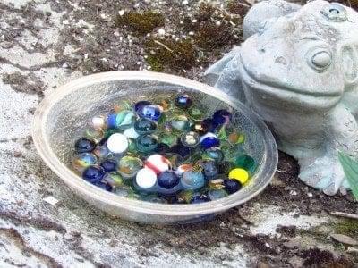 bowl full of water and marbles next to frog statue